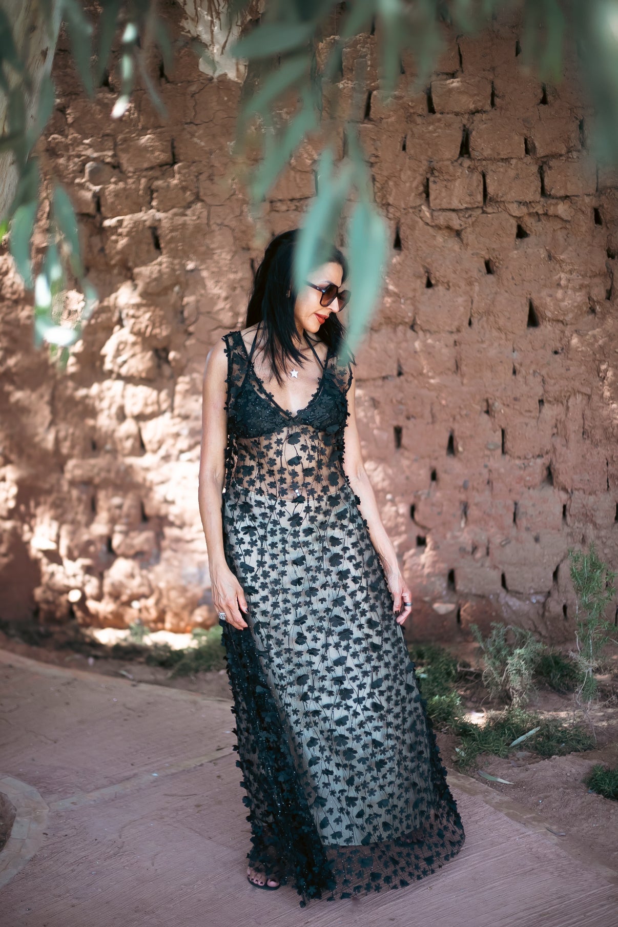 Daisy Noir embroidered sheer dress layered over a cream slip, photographed against a textured terracotta wall