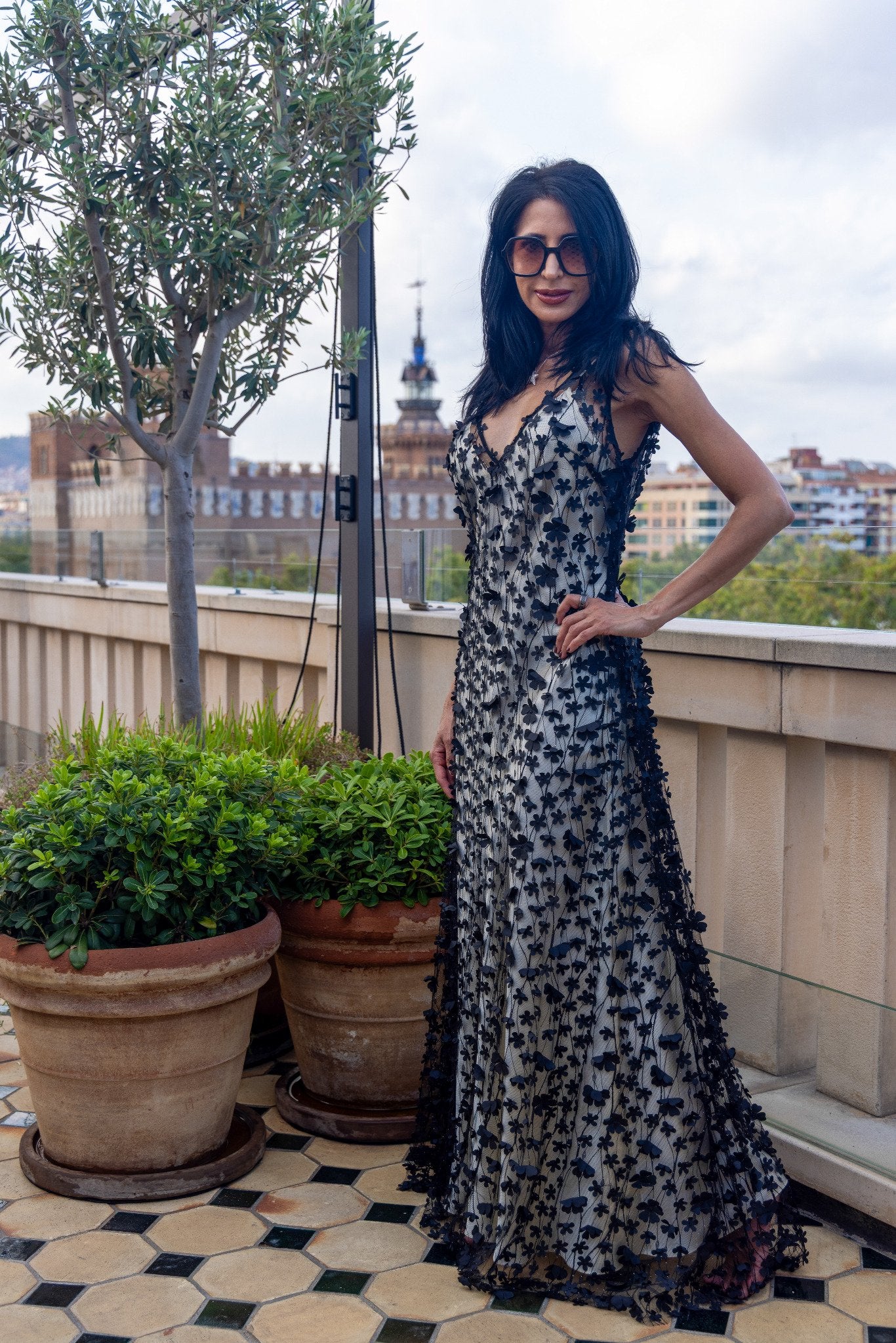 Daisy Noir by Preema Aura styled over a cream satin slip, showing the black 3D floral appliqué and elegant full-length silhouette on a rooftop terrace.