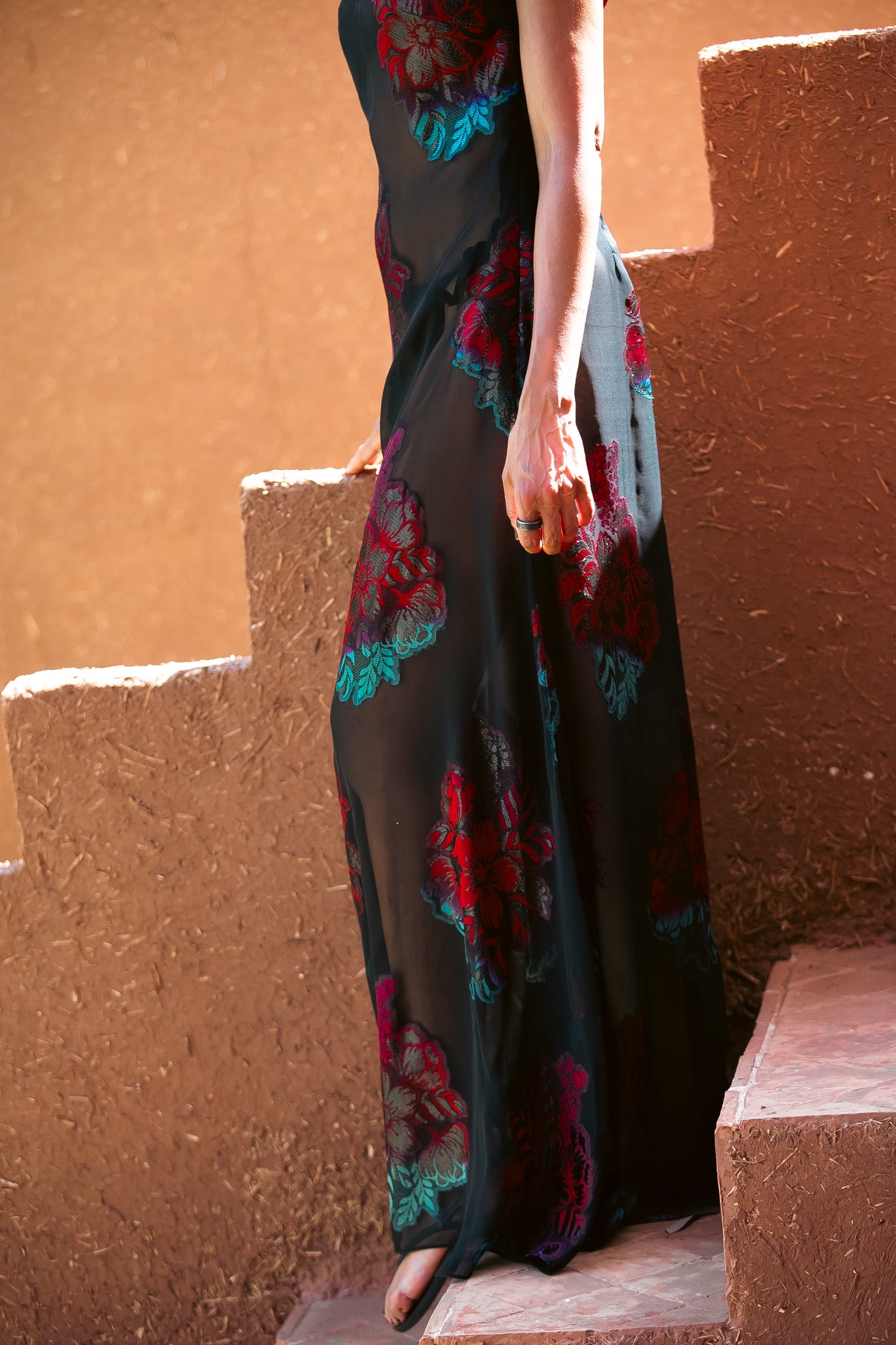 Detail shot of the Dusky Rose sheer floral gown in motion, showing embroidered hibiscus motifs on flowing black fabric