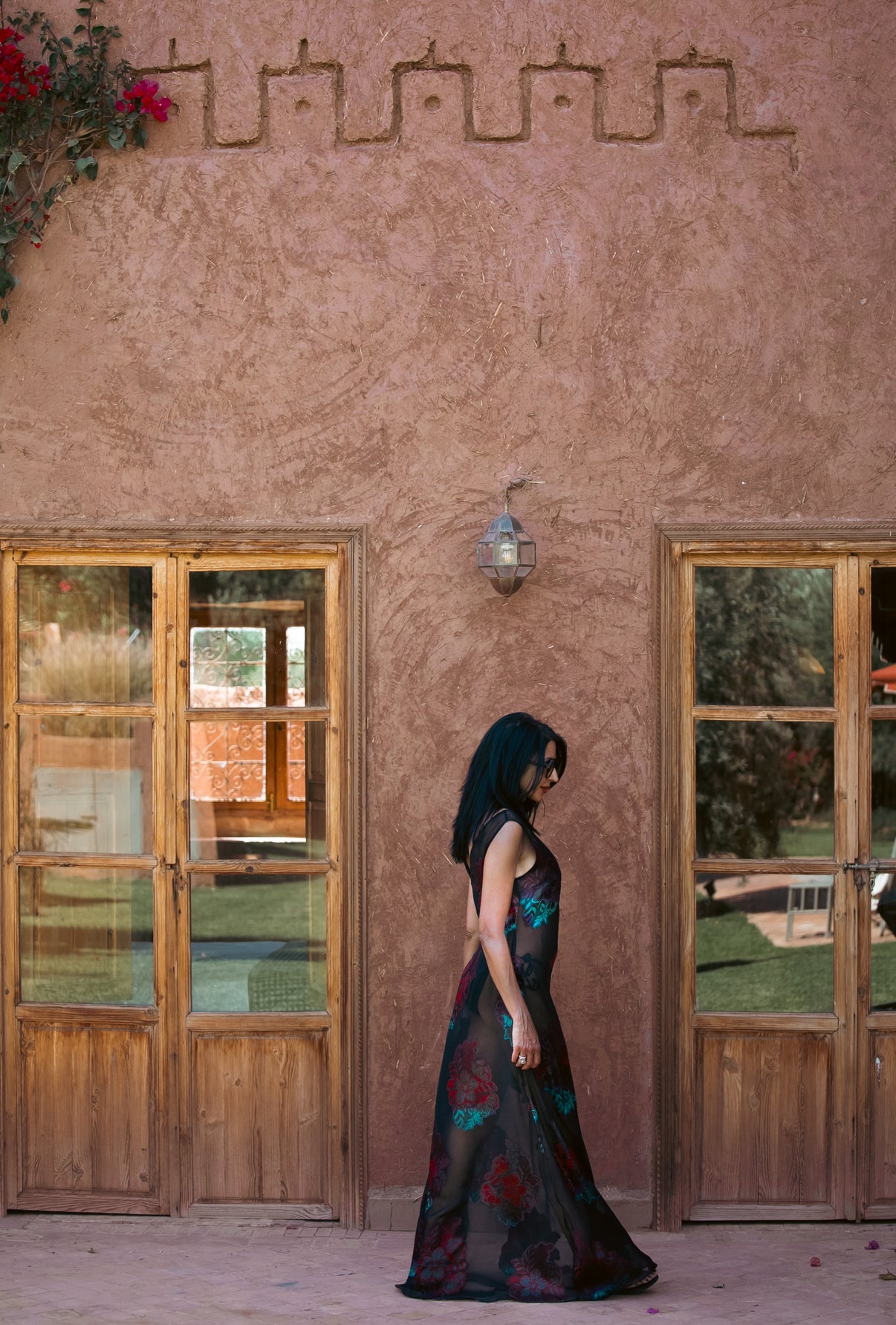 Side view of the Dusky Rose sheer black gown with red and teal floral embroidery, photographed against an earthy Moroccan wall