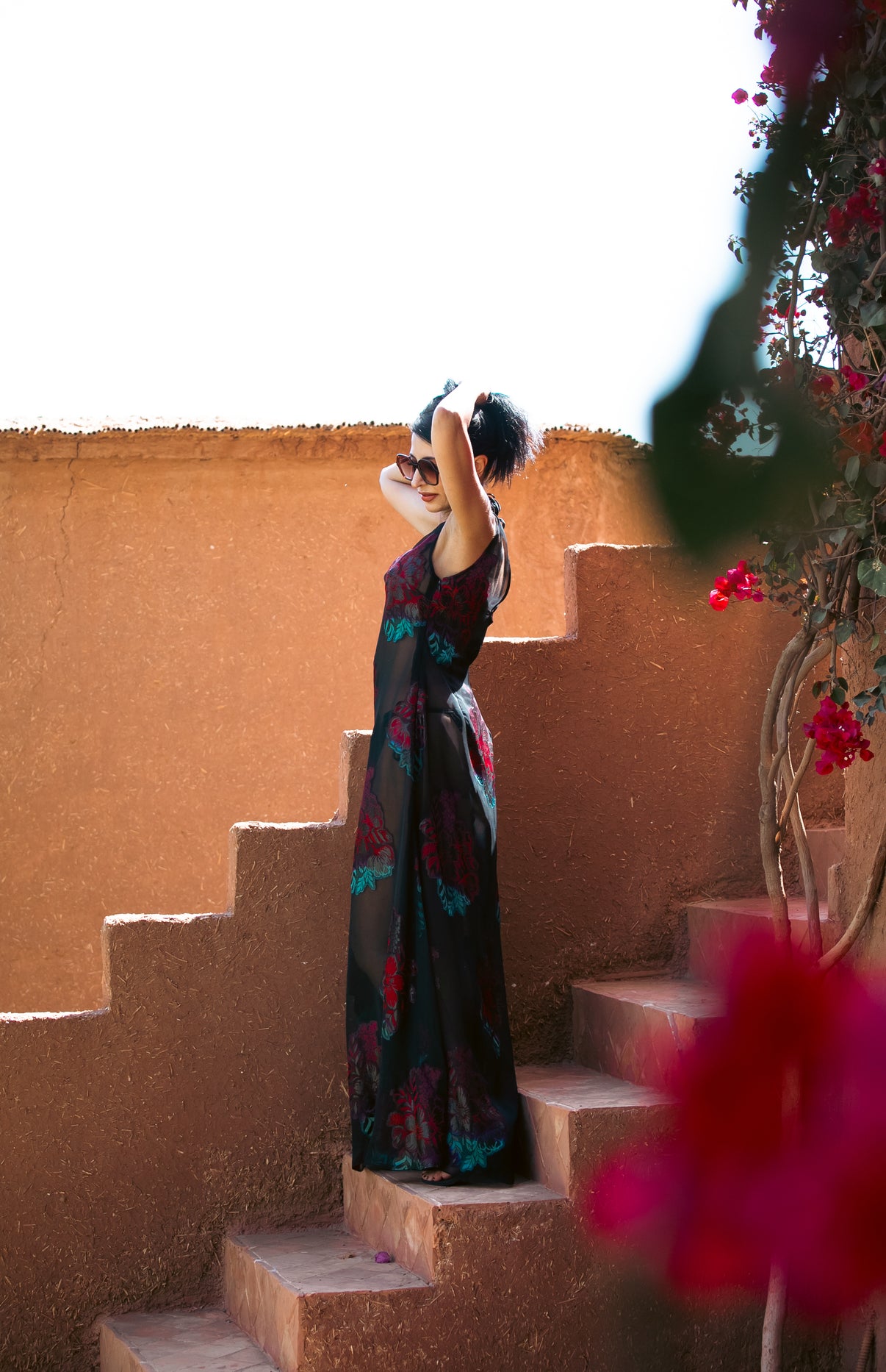 Artistic shot of model wearing the Dusky Rose embroidered gown on terracotta steps, framed by bougainvillea flowers