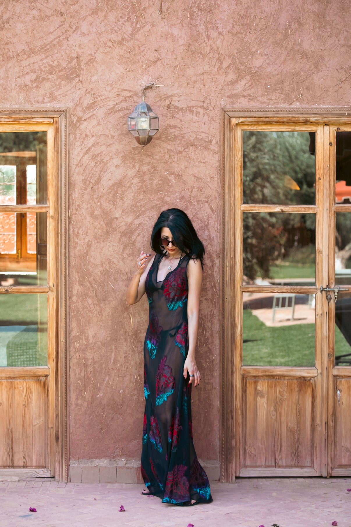 Woman in a colorful dress standing in front of a rustic building with wooden doors.