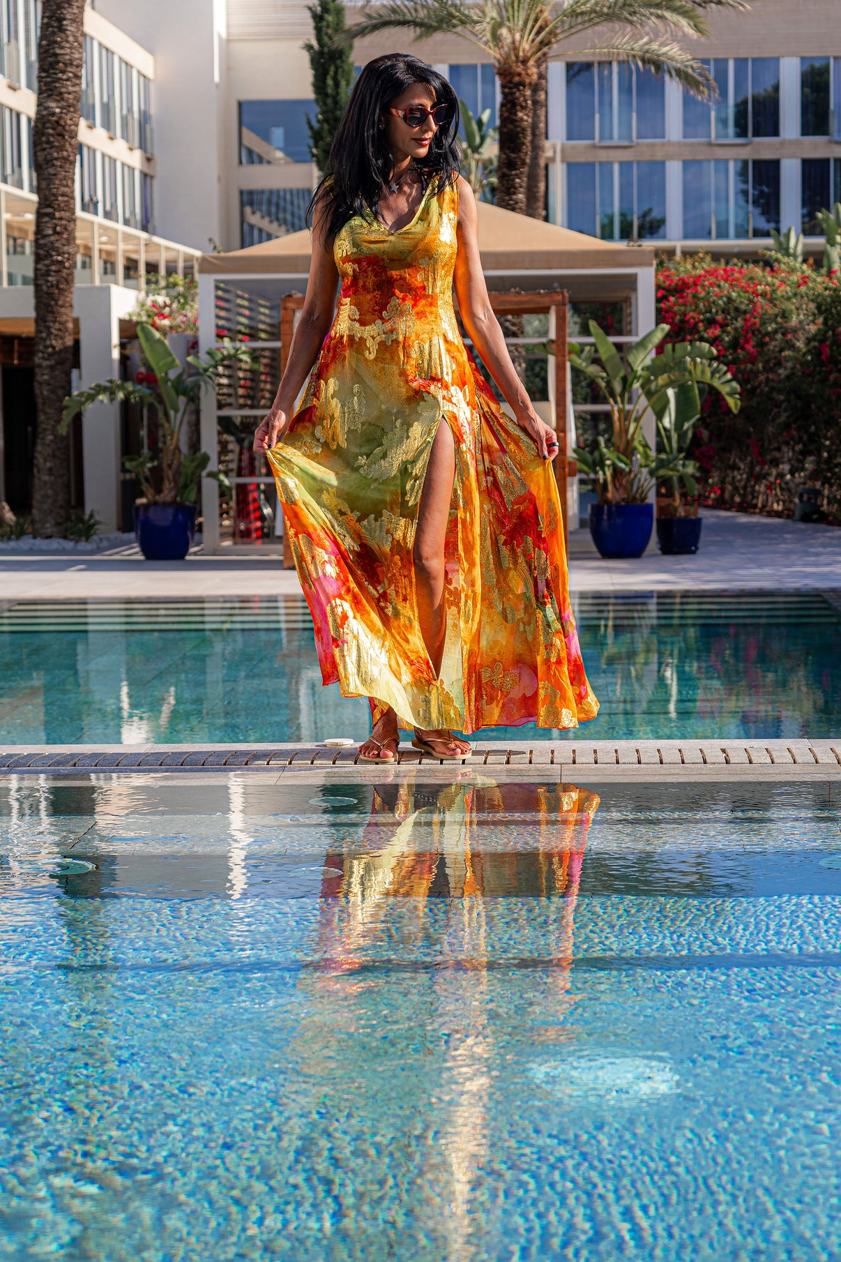 A woman in a bright yellow dress with gold, red and orange accents, standing by a swimming pool