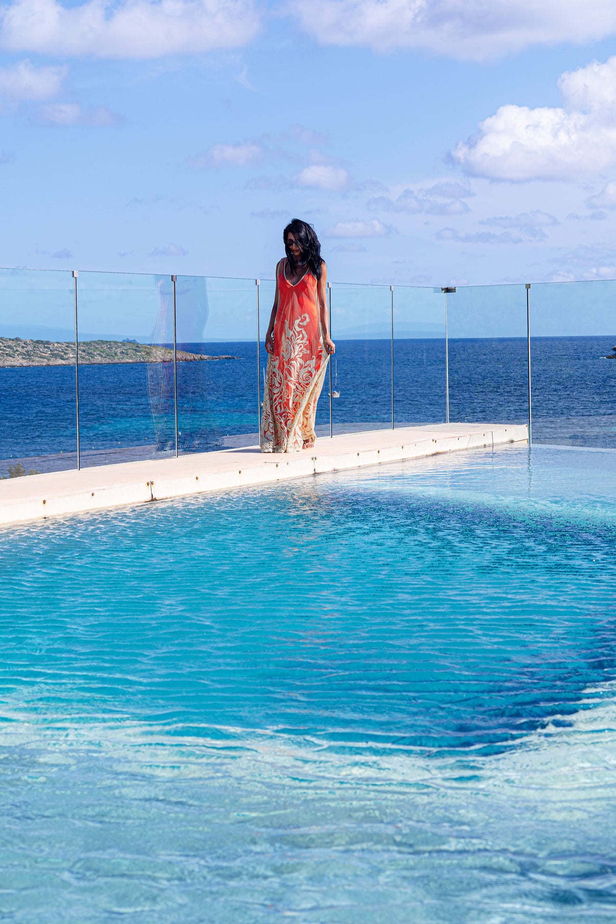 Citrine Essence dress with a red satin slip underneath, flowing gently in the breeze as the model walks along the water’s edge.