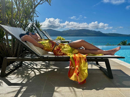 Model laying on a sun lounger next to a swimming pool, in the Mystique Horizons dress, evoking dreamy resort style.