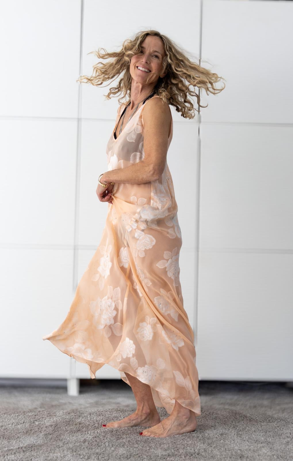 Woman wearing the Soul Bloom dress by Preema Aura, a sheer peach maxi with soft white floral embroidery from the Soul Series collection, captured in motion to highlight its lightweight, flowing fabric and feminine resortwear style.