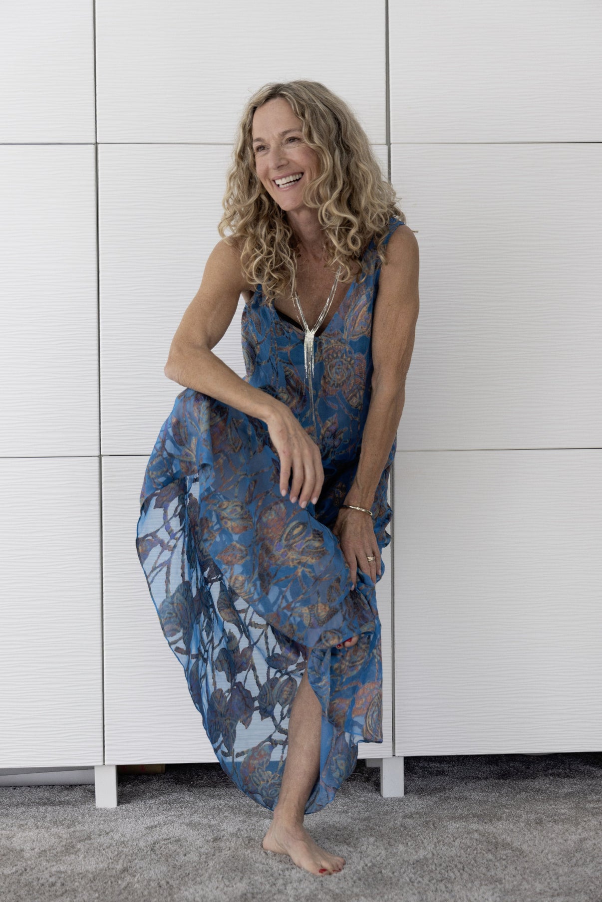 Woman wearing the Preema Aura Soul Drift blue sheer silk maxi dress with copper floral pattern, photographed indoors in natural light, embodying effortless luxury resortwear from the Soul Series collection.
