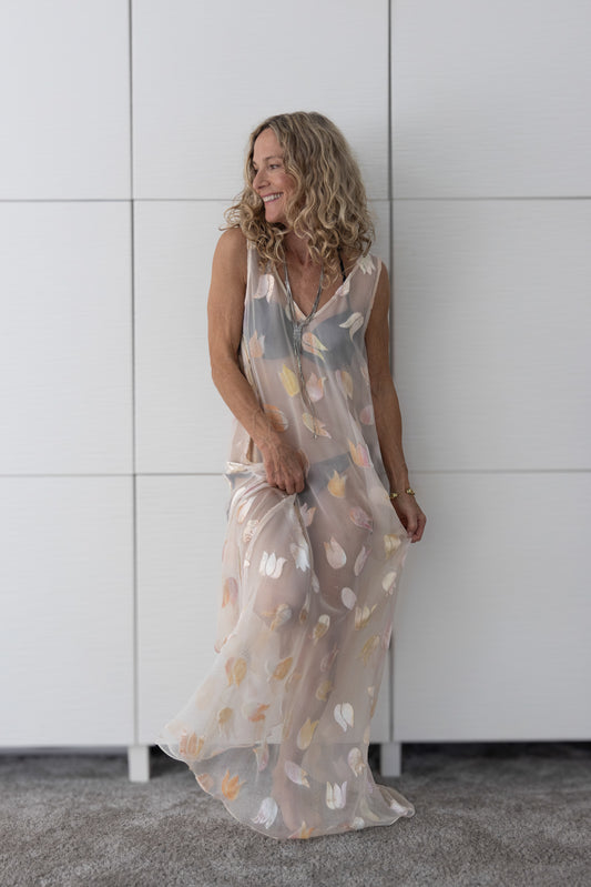Soul Glimmer by Preema Aura worn over a bikini — a sheer, lightweight maxi dress with soft multi-tonal petal motifs, captured in natural light to highlight its fluid movement and translucent elegance