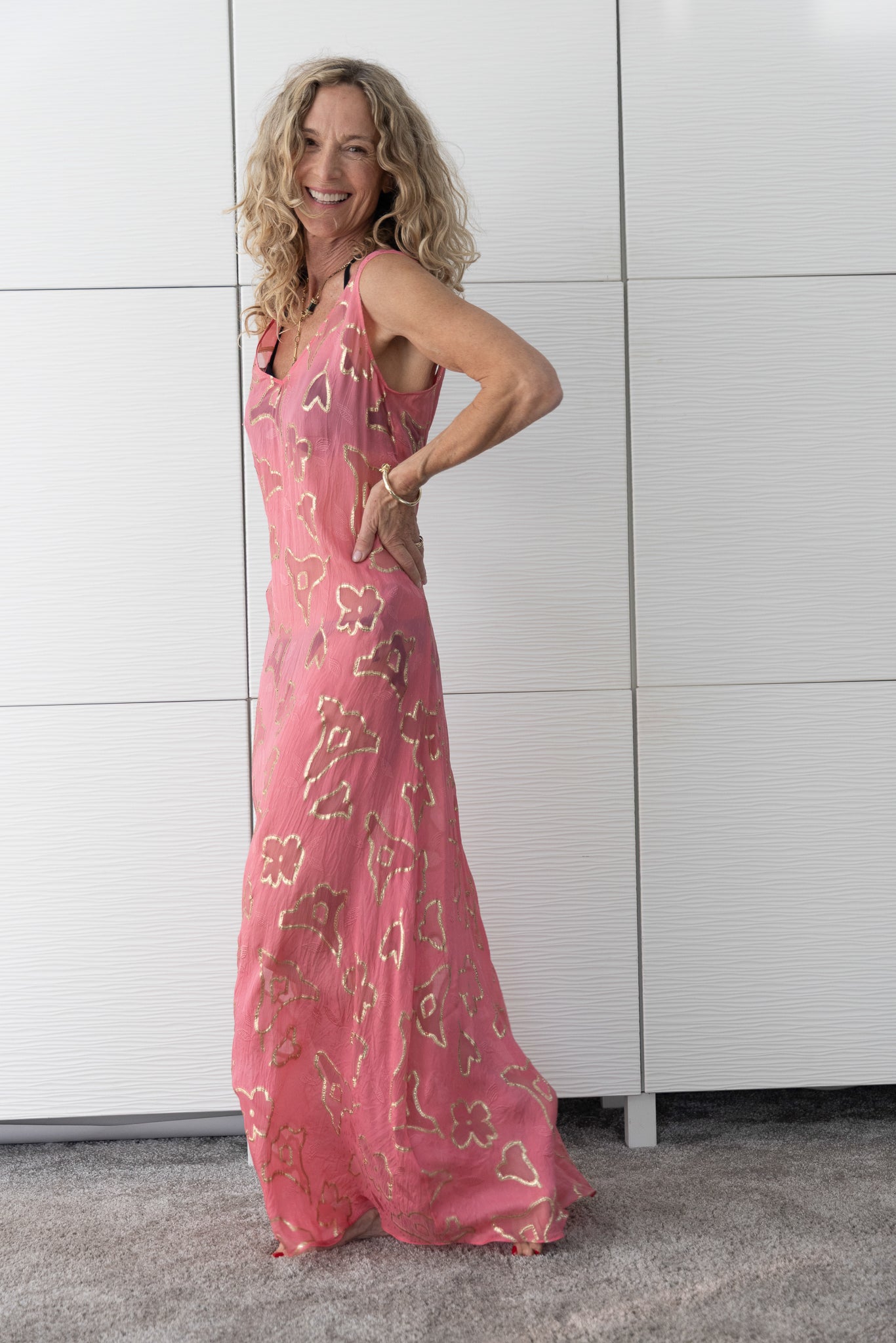 Soul Spark French silk A-line slip dress in radiant coral-pink tones, worn open over a bikini and photographed indoors in natural light to capture its luminous, sun-kissed sheen.