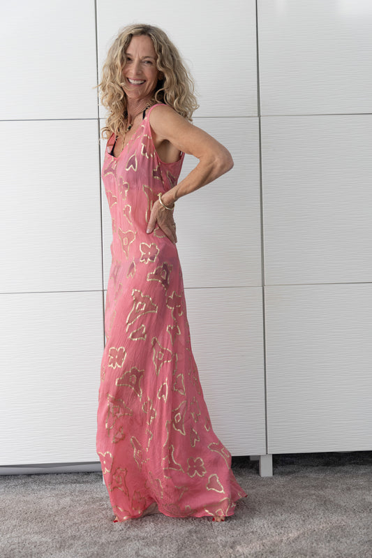 Soul Spark French silk A-line slip dress in radiant coral-pink tones, worn open over a bikini and photographed indoors in natural light to capture its luminous, sun-kissed sheen.