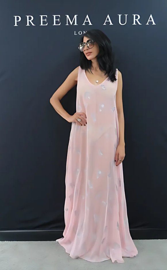 Woman wearing the Preema Aura Soul Whisper dress in soft pink silk with subtle silver embroidered motifs, standing against black branding backdrop.