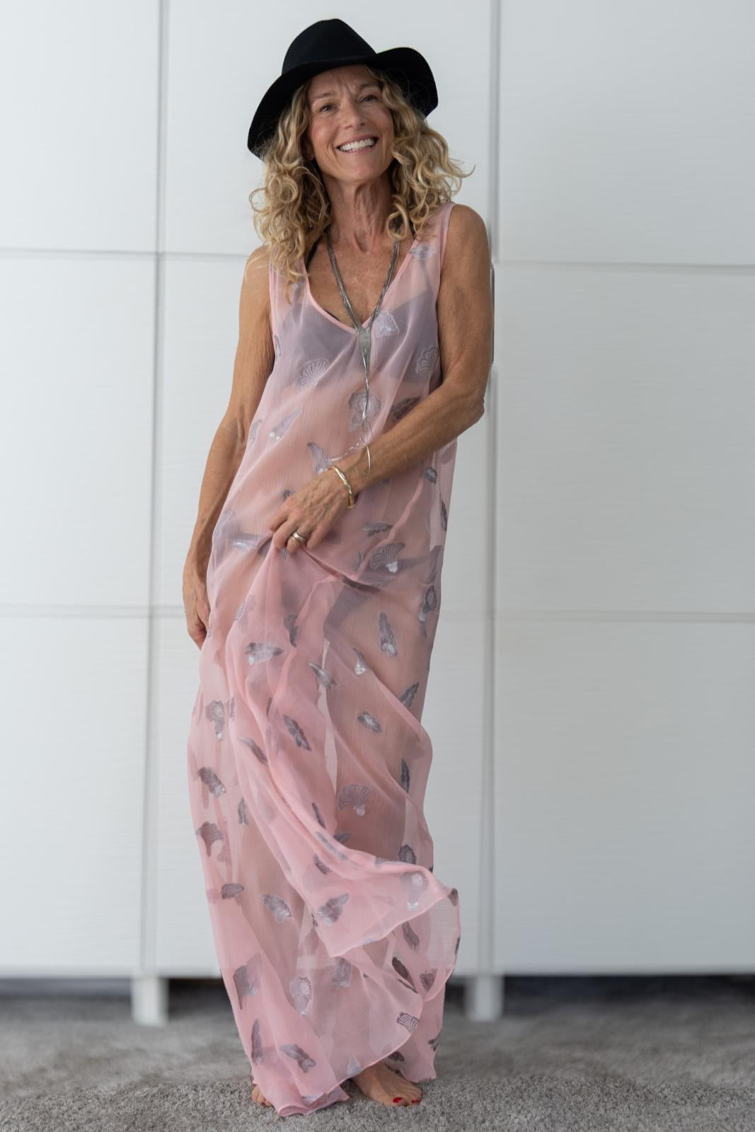 Woman wearing the Soul Whisper dress by Preema Aura, a sheer blush-pink one-off design from the Soul Series collection, styled over a bikini to highlight its light, flowing fabric embroidered with delicate silver shell motifs.