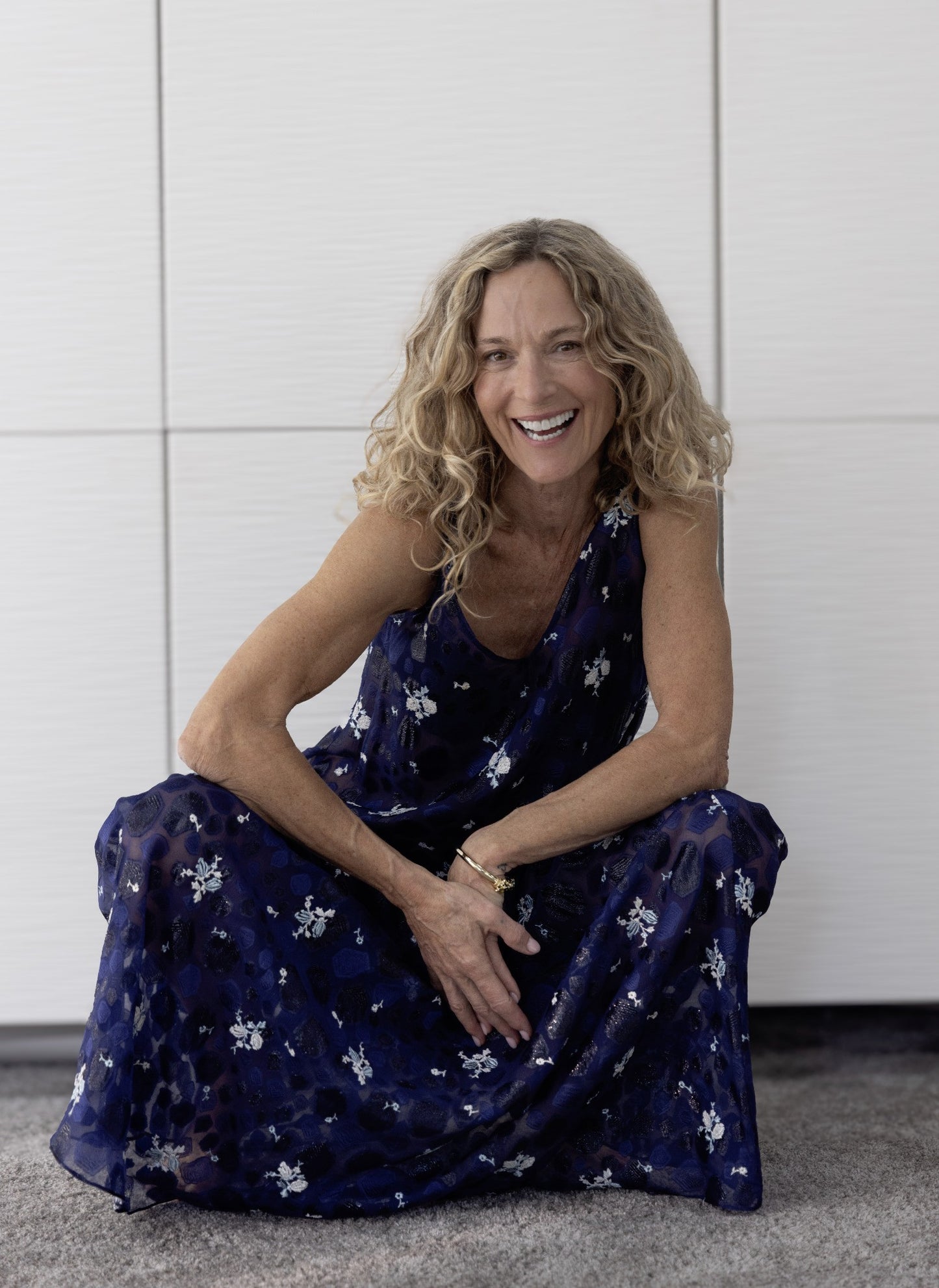 Model smiling seated in flowing Preema Aura Soul Nightfall maxi dress in midnight blue with white floral accents